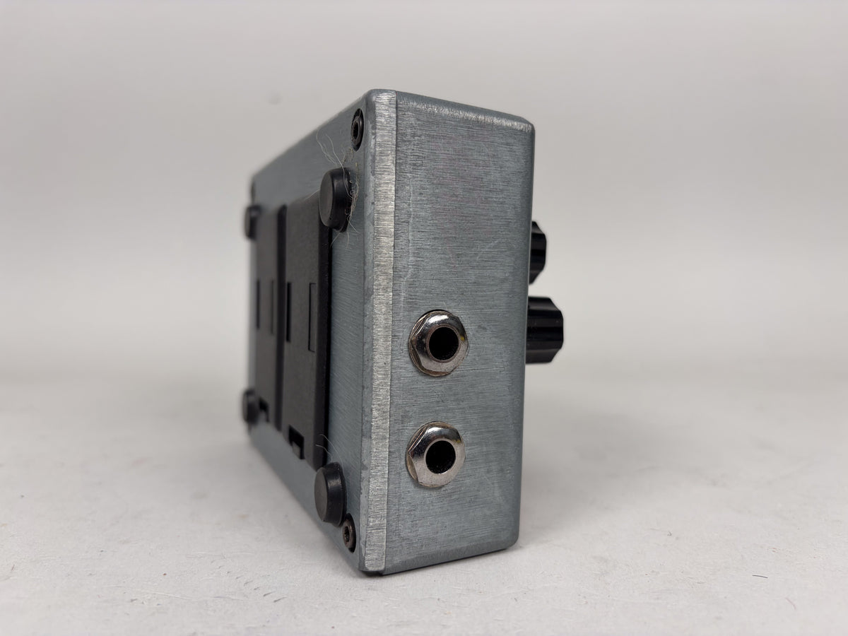 The brushed silver pedal is seen from the side, revealing two input jacks and two black control knobs.