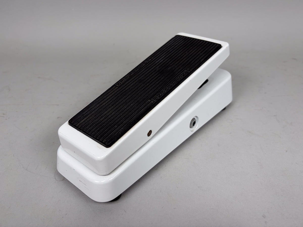 A white wah pedal, angled from the right, with a black ribbed footpad and a visible input jack on the side.