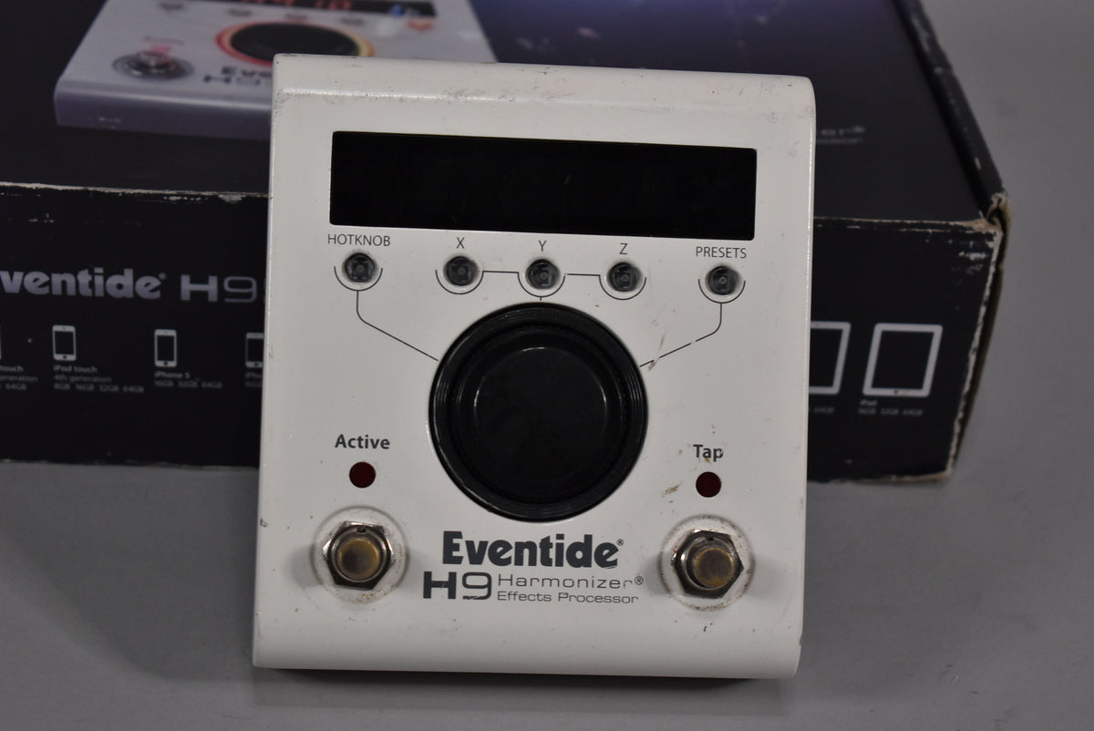 A white effects pedal with a black screen, large central black knob, five small black buttons, two red indicator lights, and two metal footswitches.