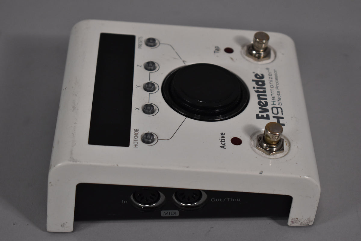 White effects pedal, viewed from the top right, showing a large black knob, two footswitches, and MIDI ports on the back.