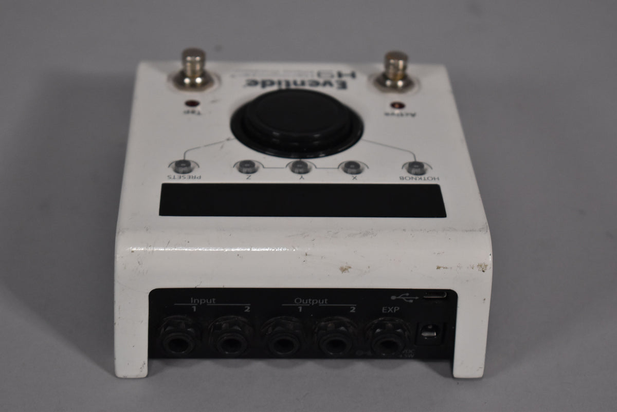 A white Eventide H9 Max pedal with two footswitches, a large black knob, five smaller buttons, a screen, and six jacks.