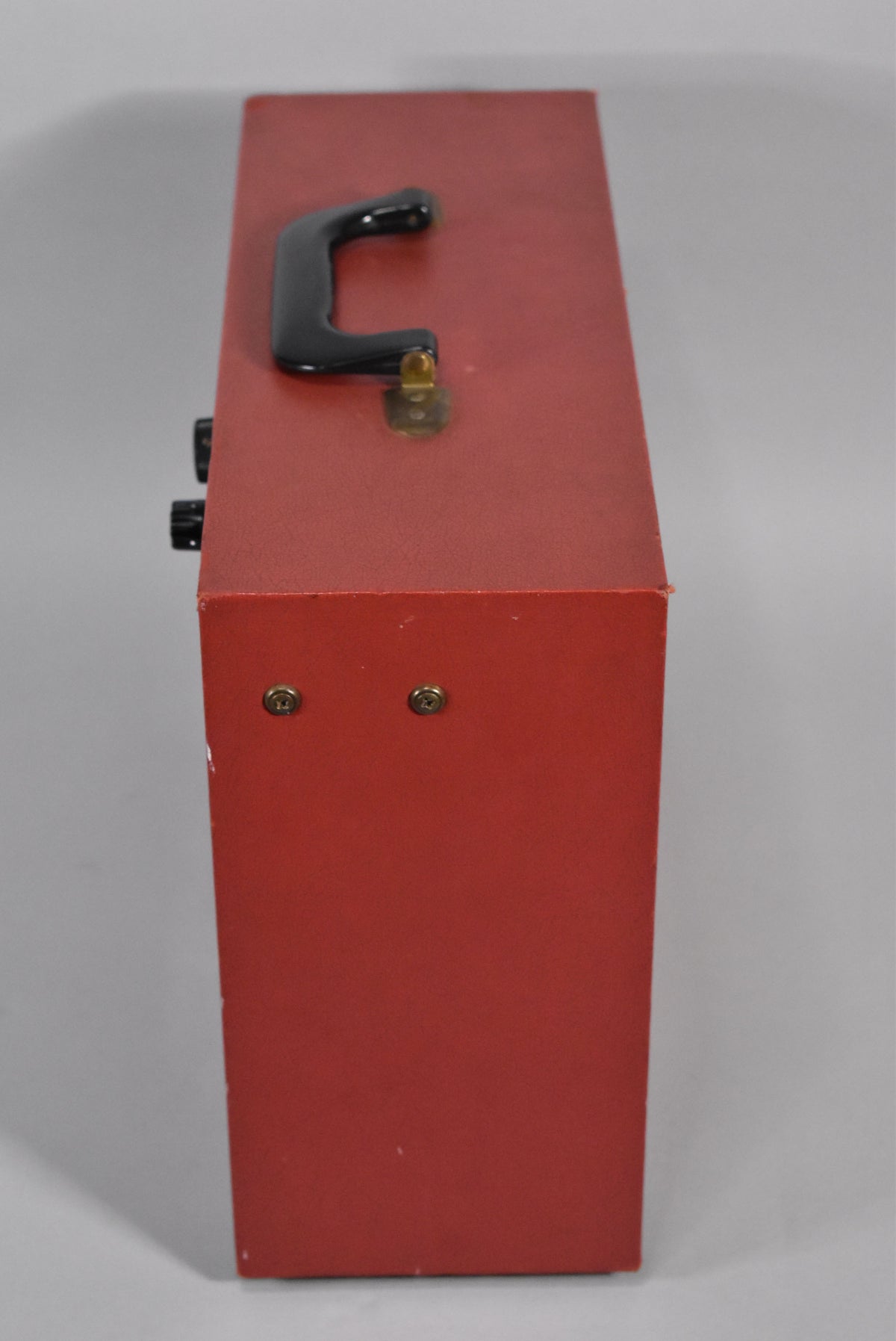 Top-down view of the red amp, showing the black handle, two control knobs, and two brass screws on the side.
