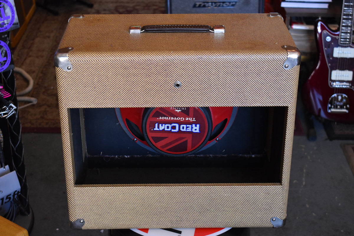 Front view of a tweed-covered cabinet with metal corner protectors, a top handle, and a visible red speaker with a Union Jack design.