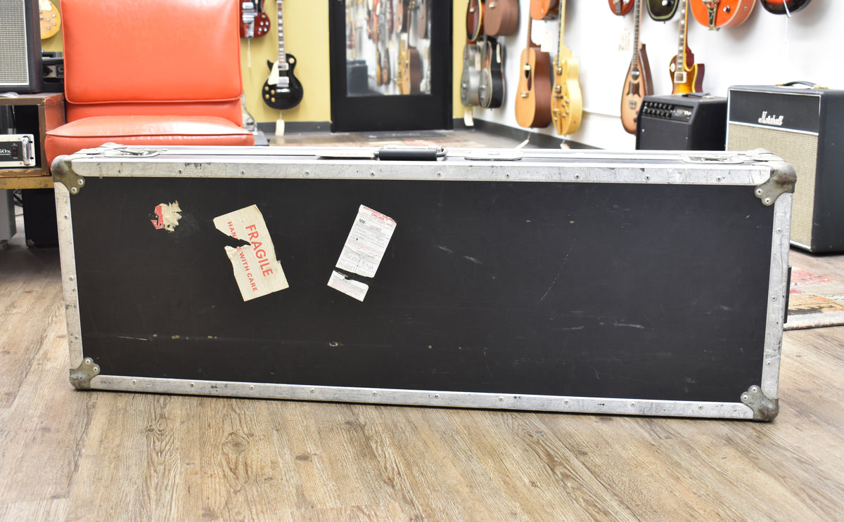 The black flight case is shown from the side, with silver metal edges, corner protectors, and two torn "Fragile" stickers.