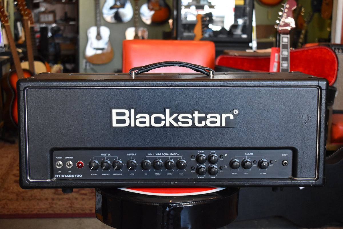 A black textured amp head, seen from the front, with a white logo, black control panel, and a top handle.