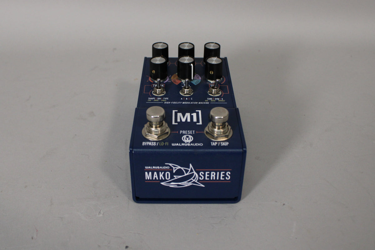 A dark blue guitar pedal, viewed from above, with two footswitches and six black control knobs on a colorful graphic background.