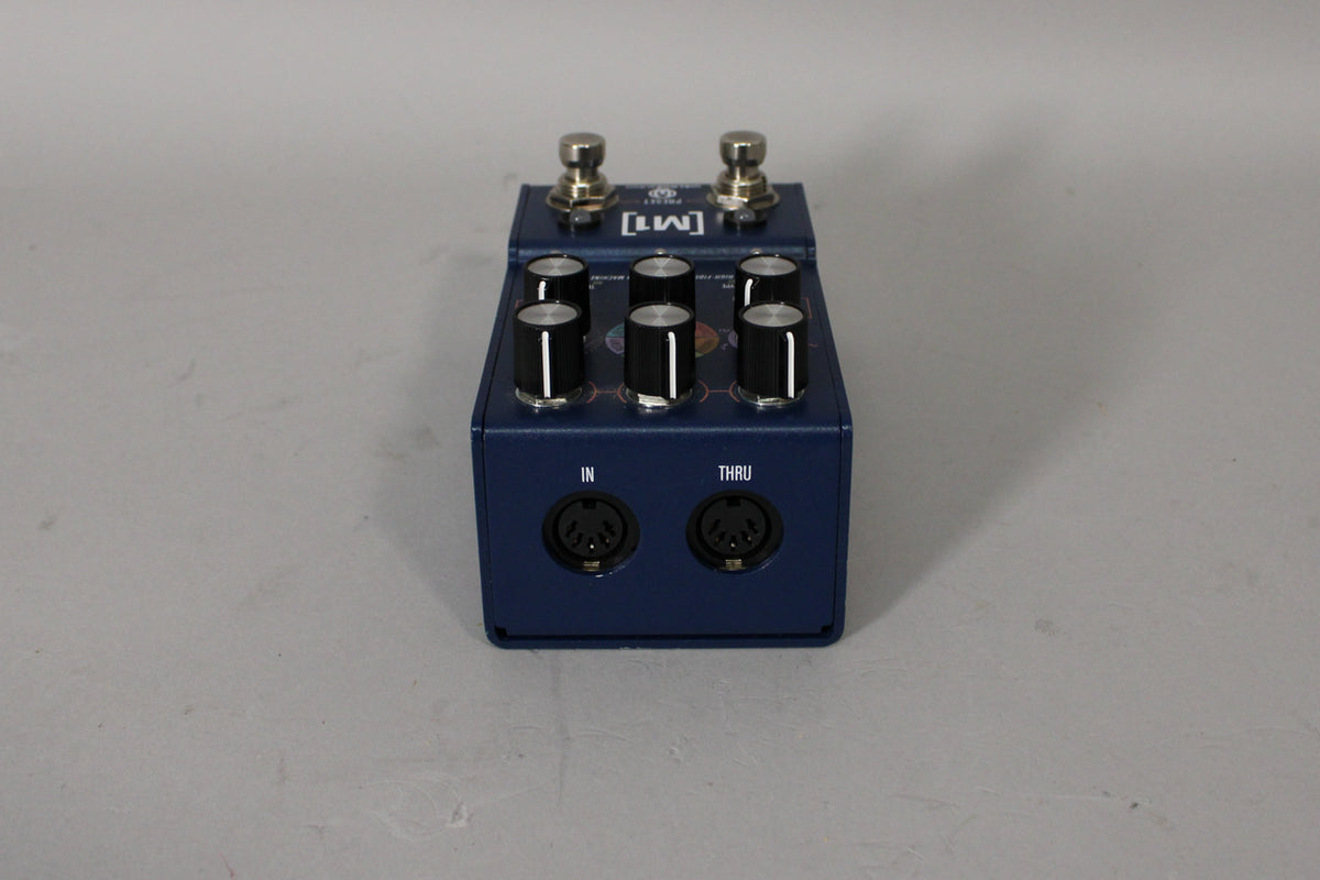 A blue Walrus Audio M1 pedal with six black knobs, two footswitches, and "IN" and "THRU" ports on the front.