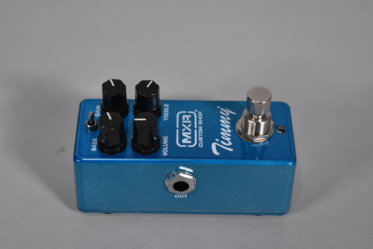 A brushed blue pedal, angled from the front-right, showing four black knobs, a chrome footswitch, and an output jack.