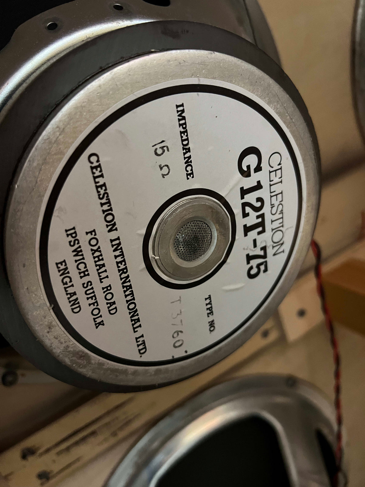 Close-up of a Celestion G12T-75 speaker, showing its silver frame, white label with black text, and a mesh dust cap.