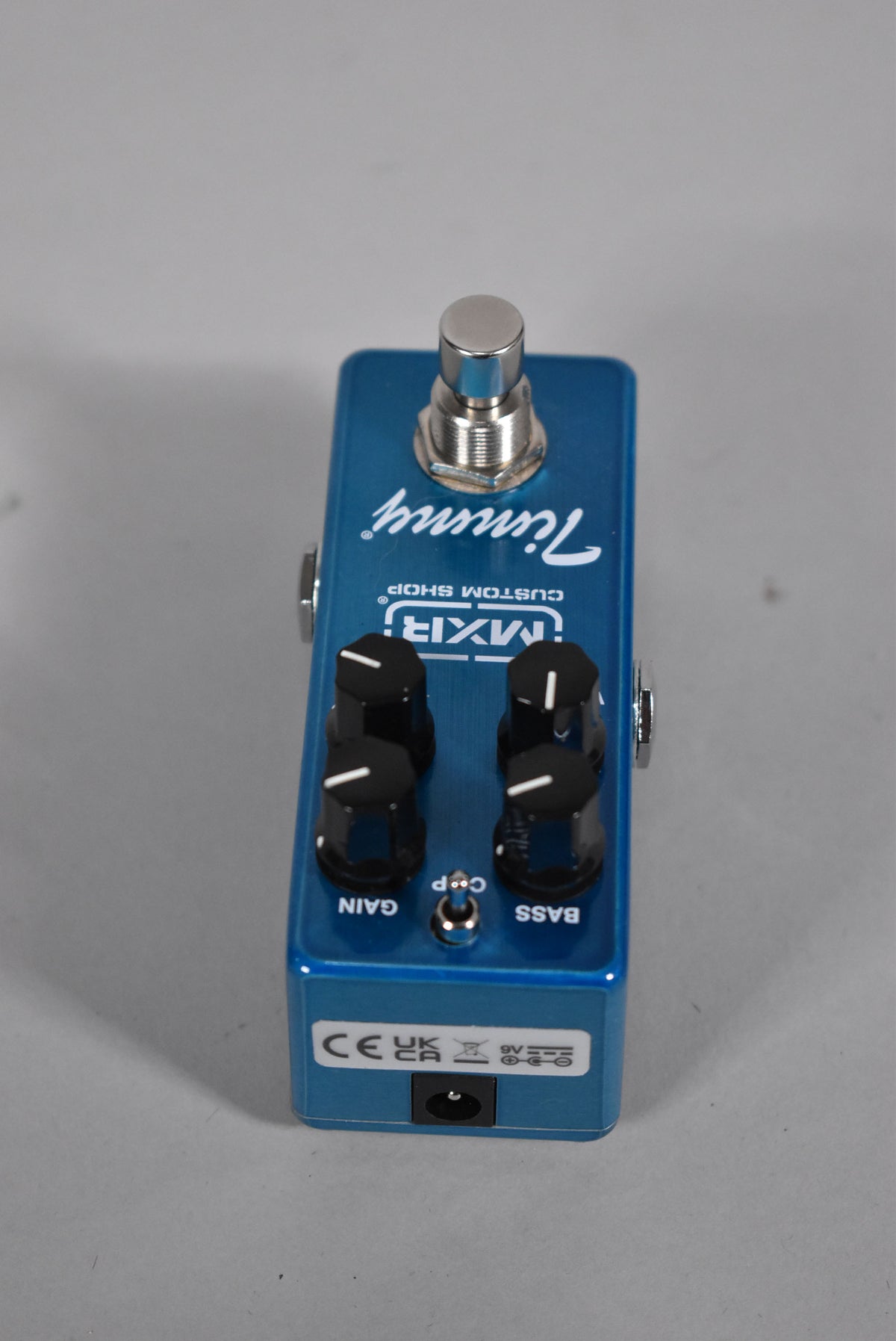A top-down view of a metallic blue pedal with a chrome footswitch, four black control knobs, and a power input jack.