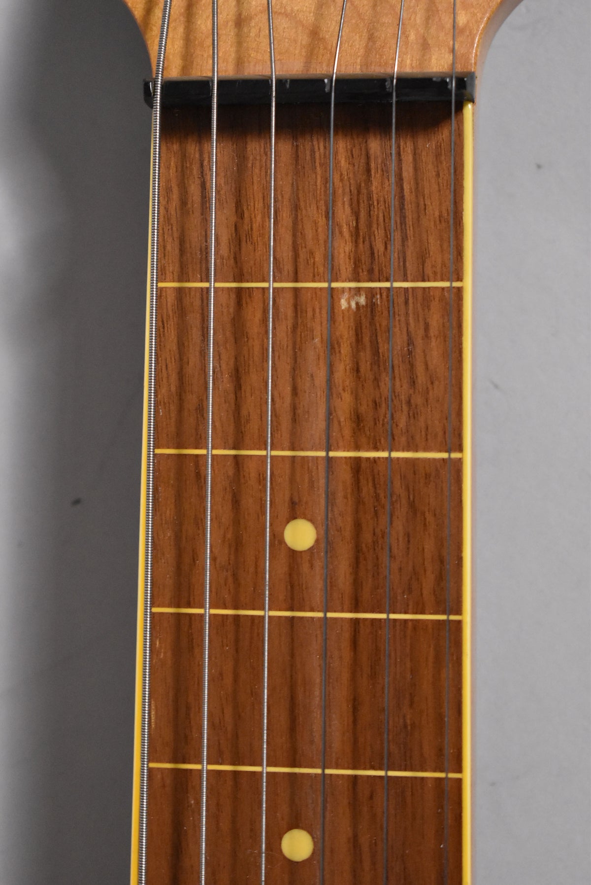 Close-up of the lapsteel's dark brown fretboard with yellow fret lines and circular inlays, showing light wear near the nut.