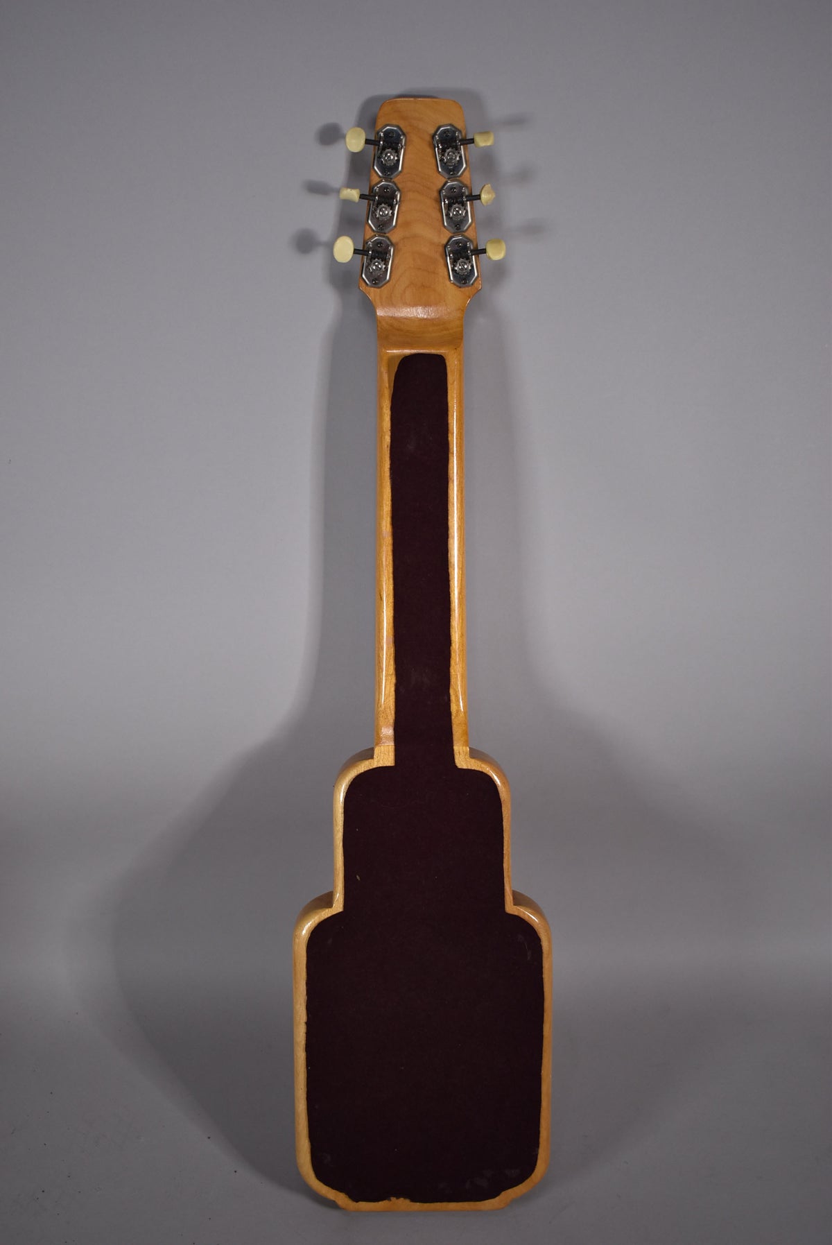 Full rear view of a light-colored wooden lap steel with a dark brown felt-lined back and six cream-buttoned tuners on the headstock.