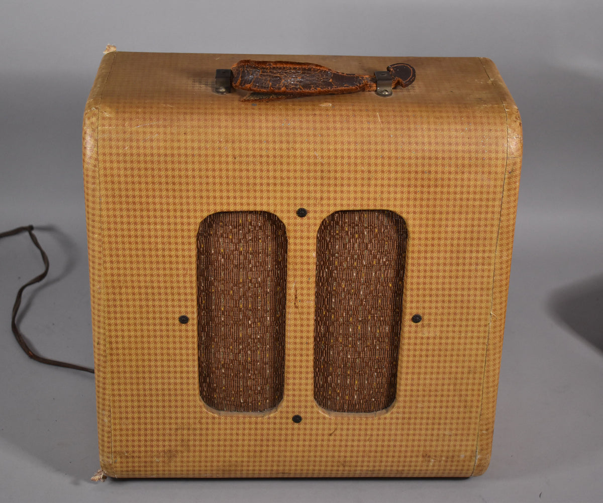 Front view of a vintage amplifier with a tan and brown checkered tweed finish, two vertical speaker grilles, and a worn leather handle.