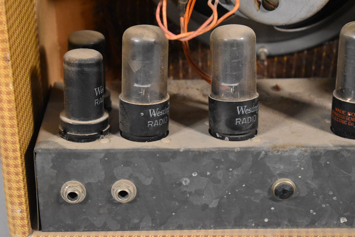 Close-up of the amplifier's dusty, worn metal chassis with four vacuum tubes and two input jacks, wires visible in the background.