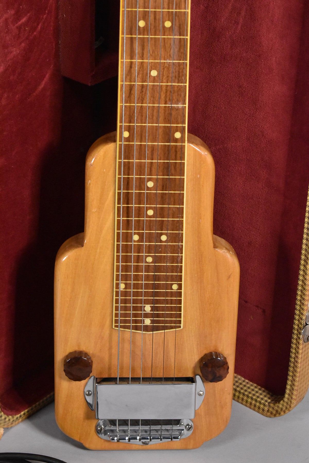 The natural finish lap steel's body and fretboard are visible, with a chrome bridge and two dark brown control knobs.
