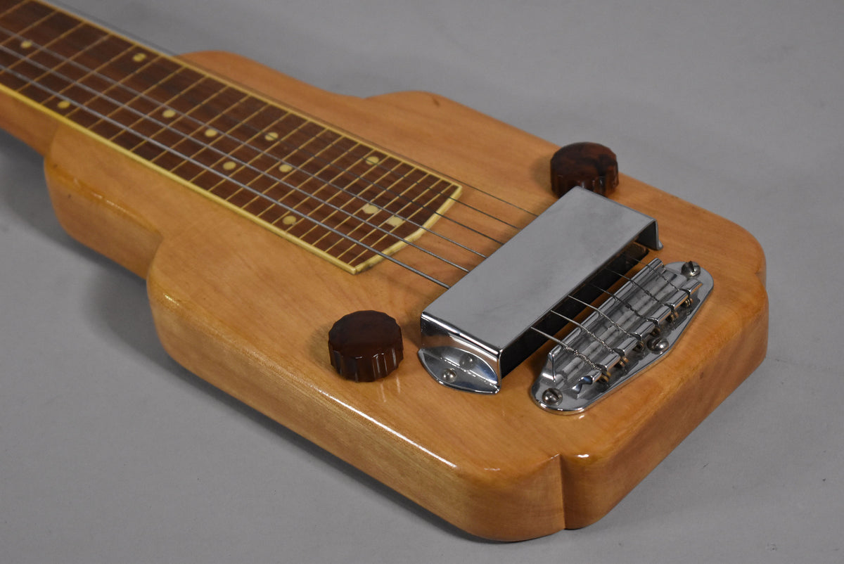Close-up of the lap steel's light wood body, showing the fretboard, chrome pickup cover, bridge, and two dark brown control knobs.