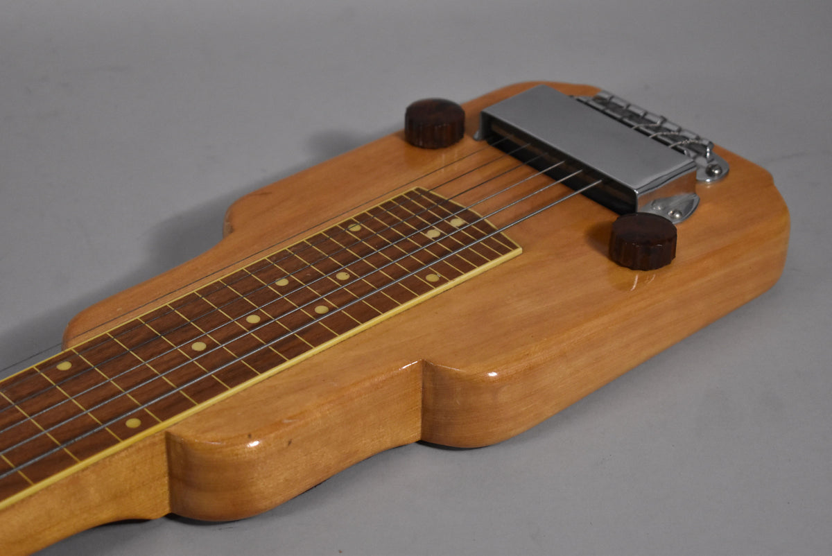 Close-up of the light brown lap steel's body, showing the dark fretboard with dot inlays, two dark brown knobs, and chrome pickup.