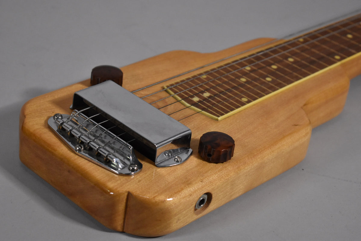 Close-up of the lap steel's light wood body, showing the chrome bridge and pickup cover, two tortoiseshell knobs, and output jack.