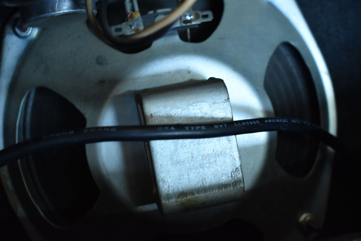 Close-up of the speaker's silver-grey magnet and frame, with a black cable running horizontally across the center.