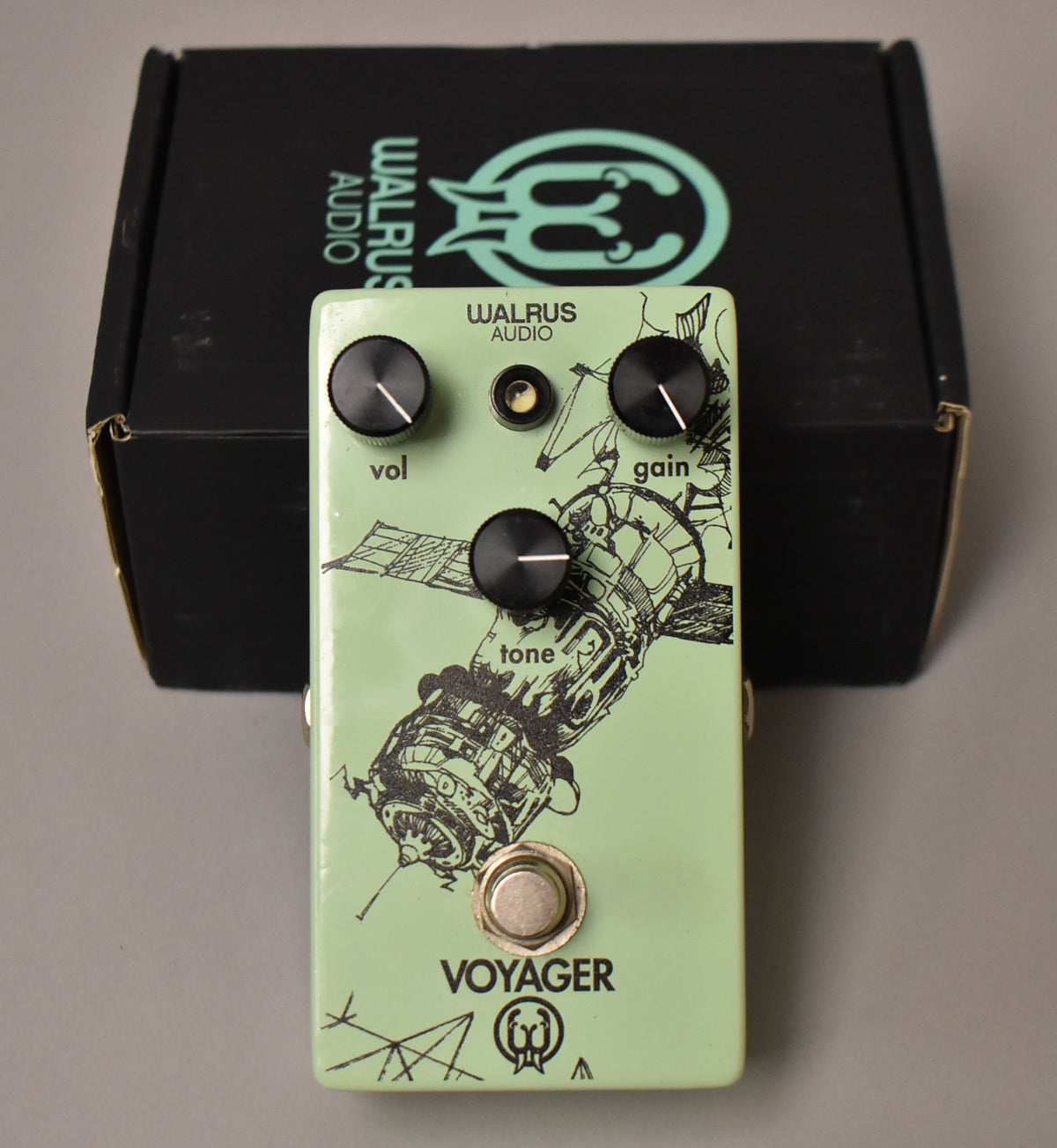 Light green effect pedal with a black line art drawing of a satellite, three black knobs, and a silver footswitch, with its box behind.