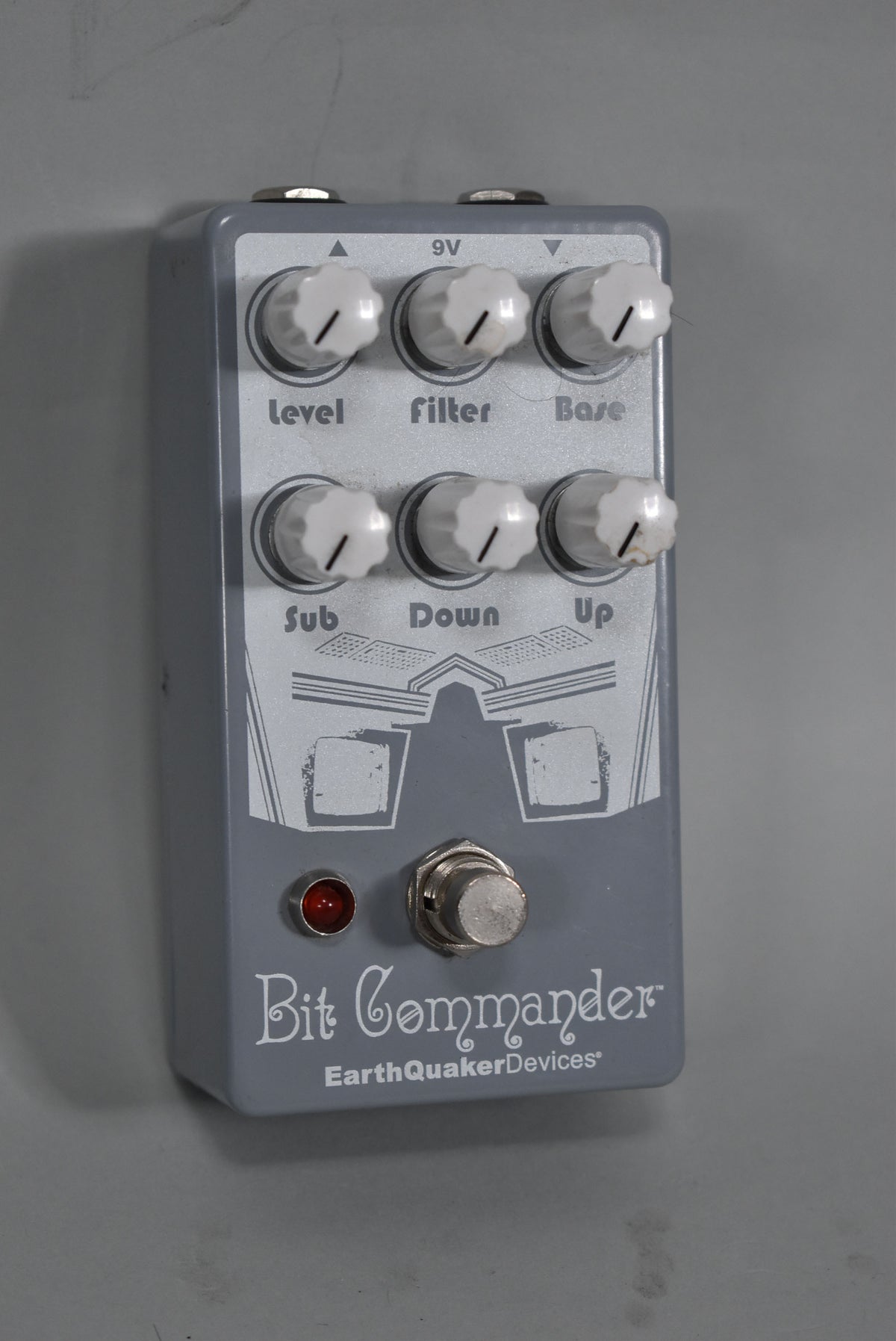 A gray effects pedal with six white knobs, a red indicator light, and a silver footswitch, viewed from a slight angle.