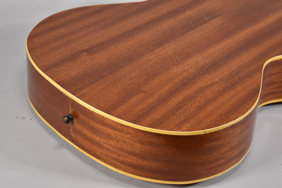 The lower bout of the natural finish acoustic guitar, showing the dark brown wood grain, light binding, and a black strap button.