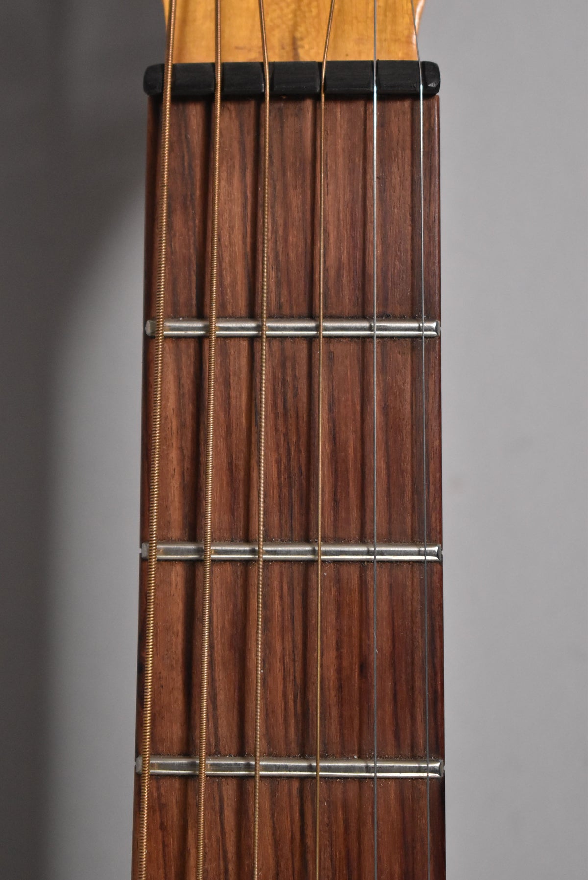 Close-up of the dark brown fretboard and nut, showing six strings, with some wear visible on the frets.
