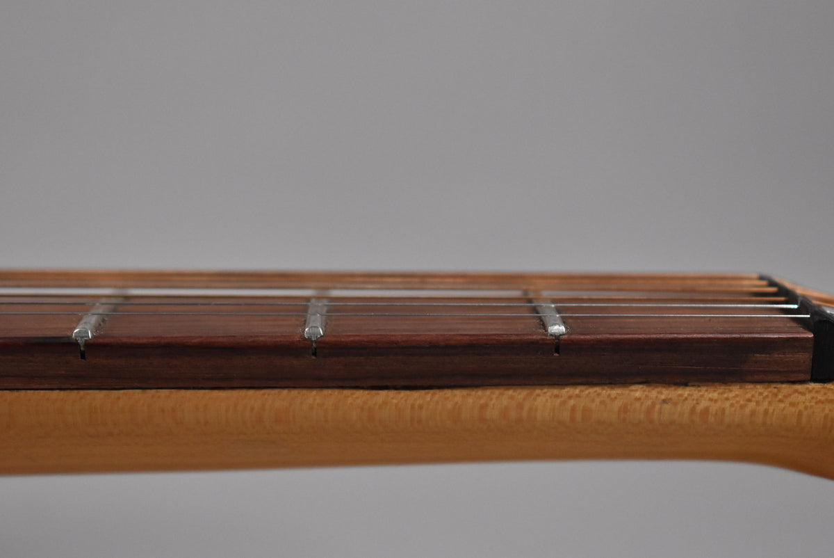 Close-up of the natural finish neck and dark fretboard, showing the strings and frets from a low angle, with some fret wear.