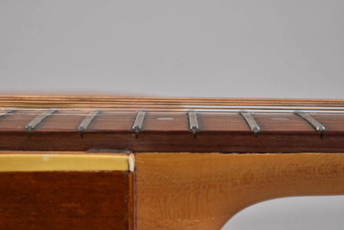 Close-up of the guitar's natural finish neck and dark fretboard with silver frets, showing light wear and a small chip on the nut.