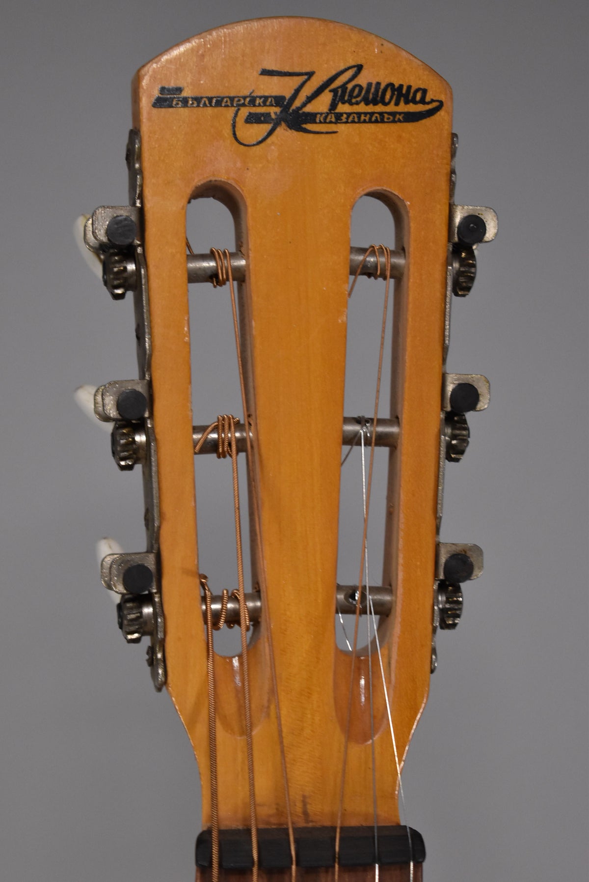 Close-up, top-down view of the guitar's light-brown headstock with open tuners, white buttons, and a black logo.