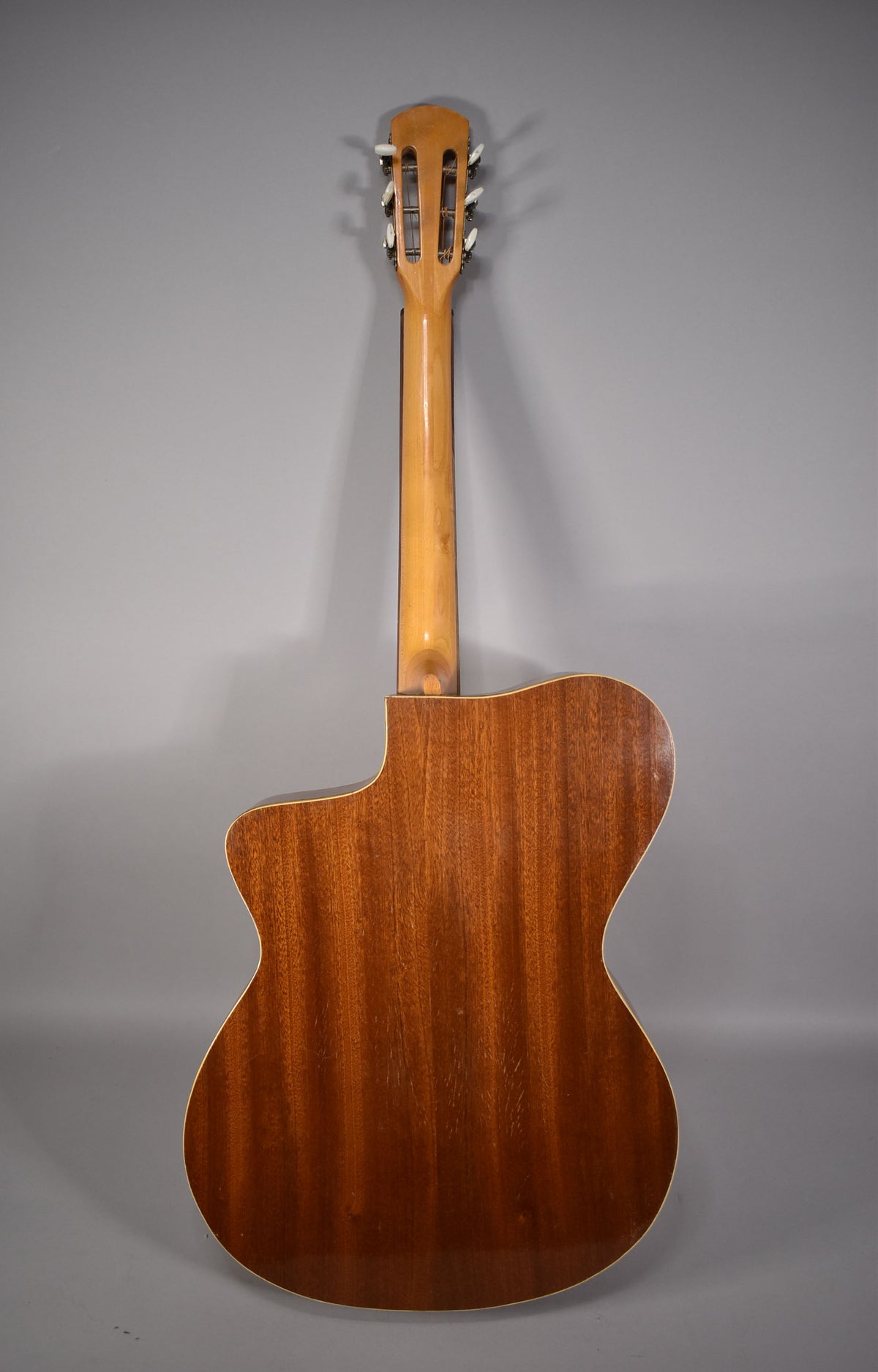 The back of the natural finish acoustic guitar shows a cutaway body, wood grain, and a light-colored neck with open-gear tuners.