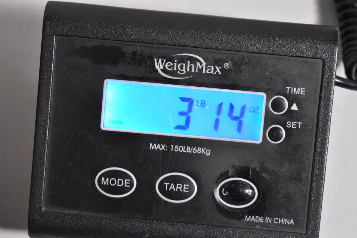 Close-up of a black digital scale displaying "3 LB. 14 OZ." in blue, with "WeighMax" and control buttons visible.