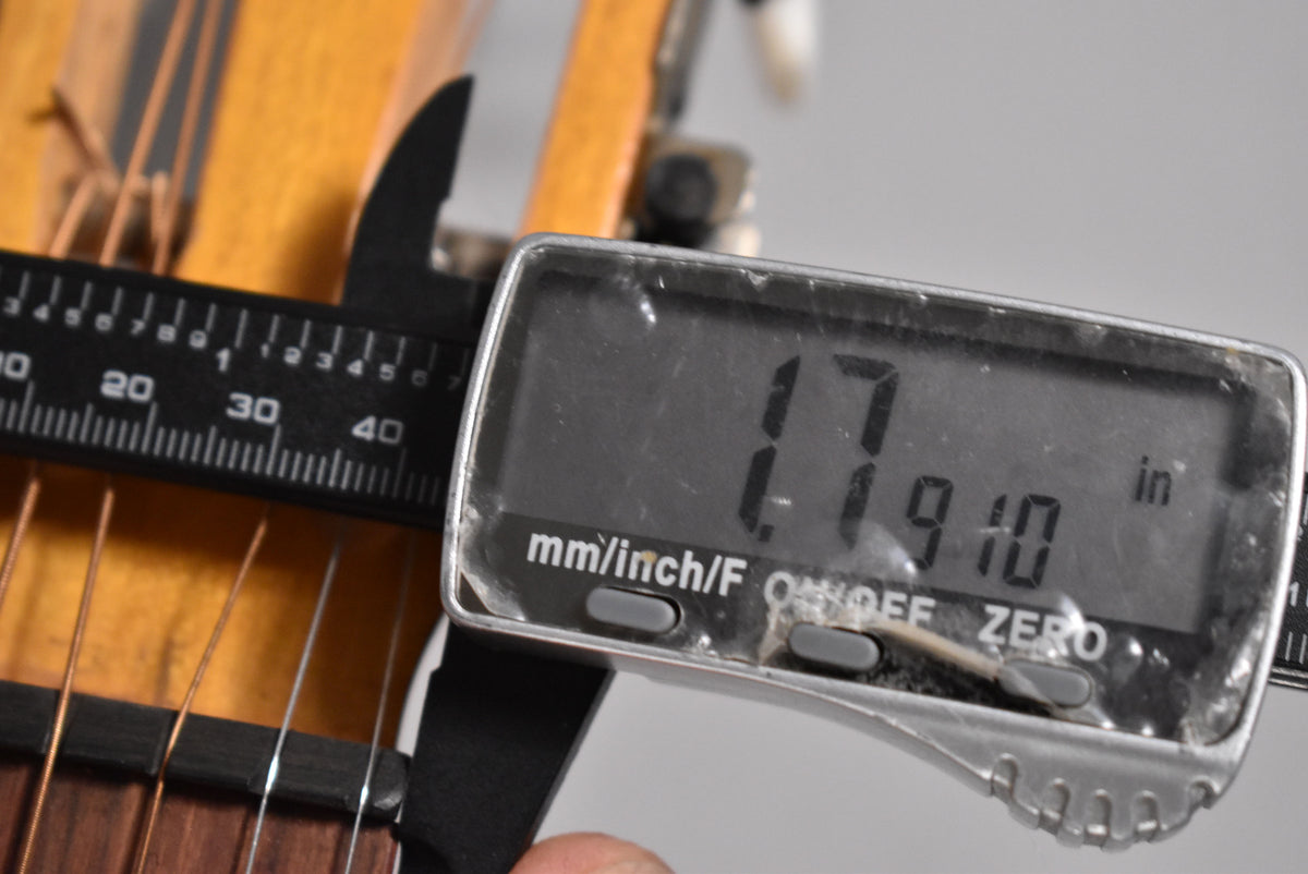 A close-up of the guitar's nut and fretboard, with a digital caliper measuring the nut width at 1.7910 inches.