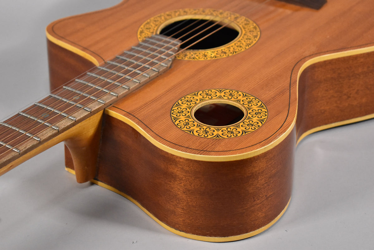 The natural finish acoustic guitar's body and neck are angled, showing two soundholes with ornate yellow and black floral rosettes.