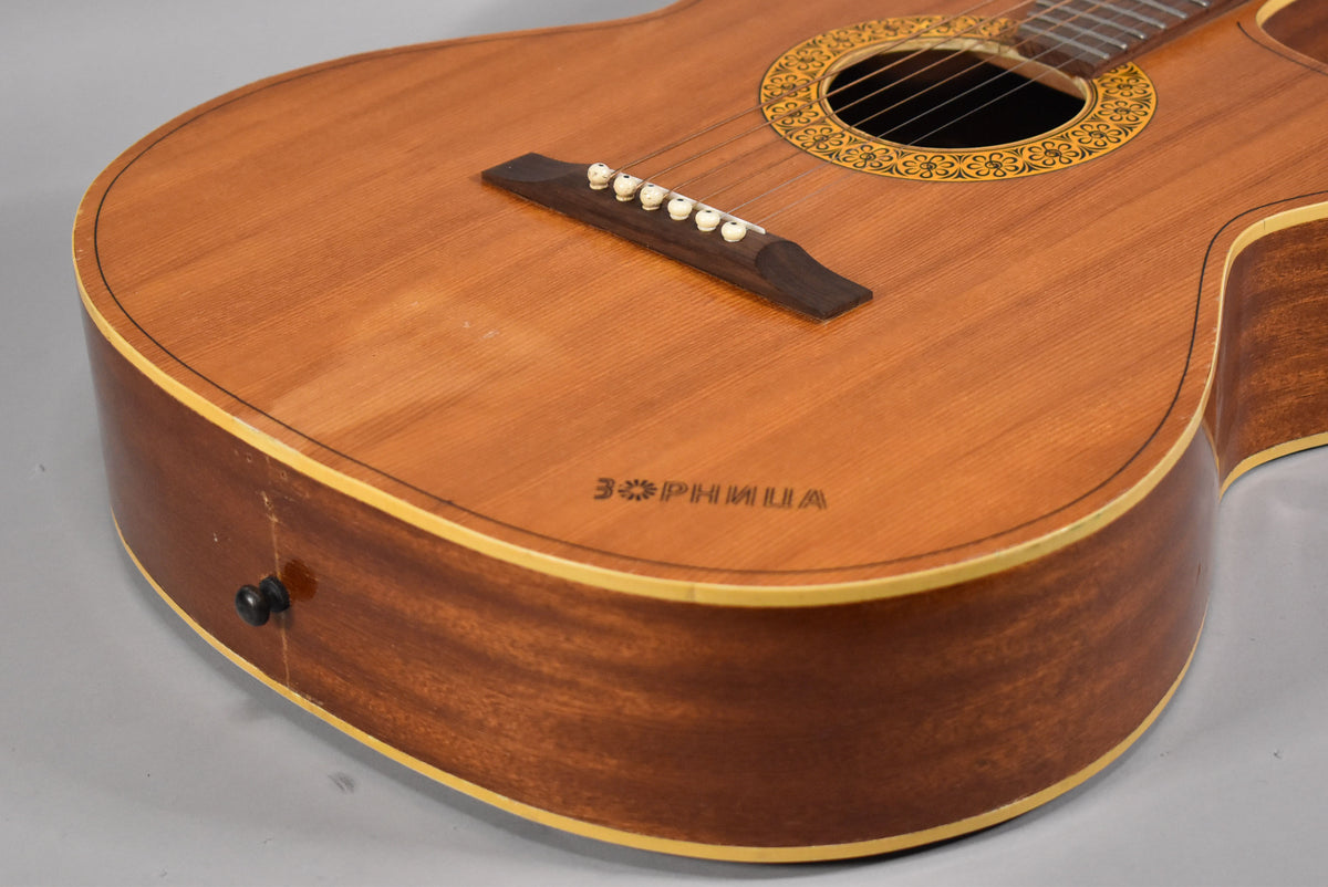 Close-up of the lower bout of a natural finish acoustic guitar, showing the bridge with white pins, soundhole rosette, and a strap button.