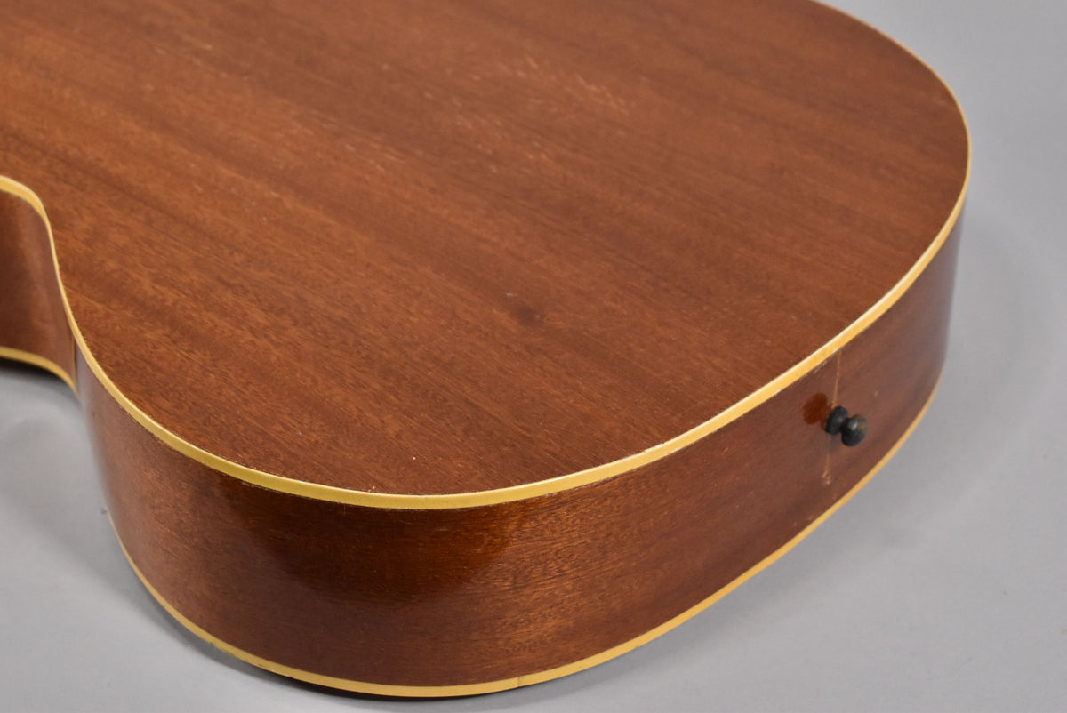 Close-up of the guitar's lower bout, showing the natural wood grain, light binding, and a black strap button on the side.