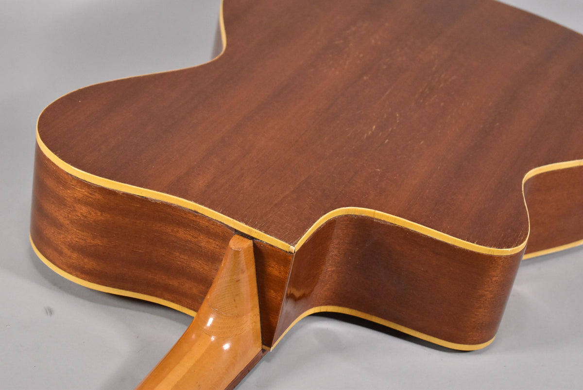 The back of the natural finish acoustic guitar shows a light-colored neck heel joining the dark brown body, with light binding.