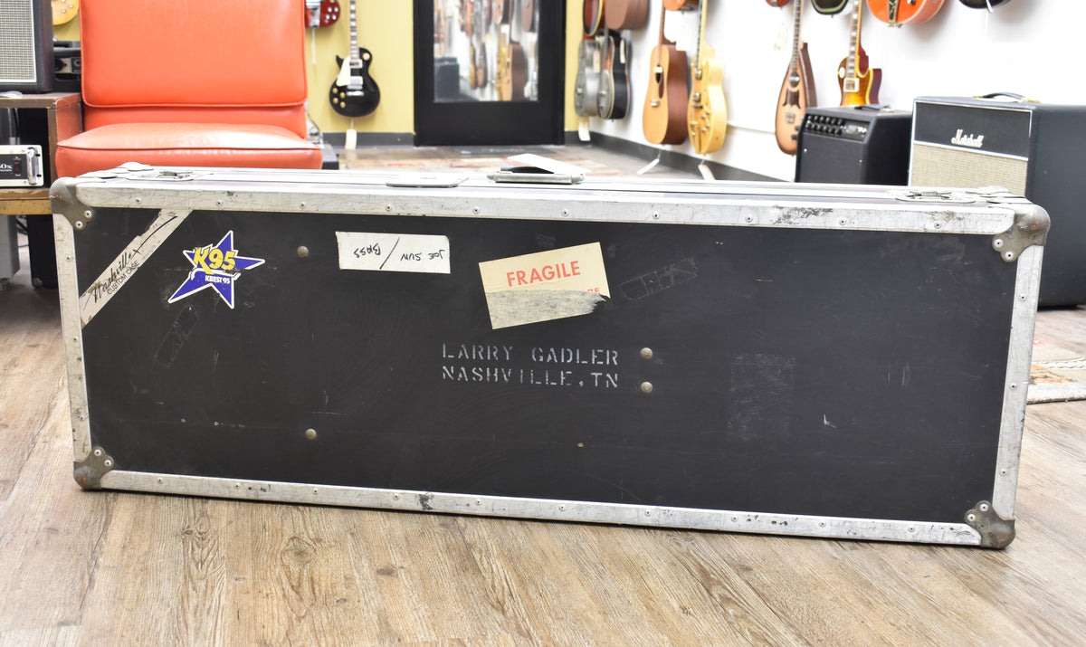 A well-worn black flight case with silver metal trim and corner protectors, covered in various stickers and stenciled with "LARRY GADLER NASHVILLE.TN".