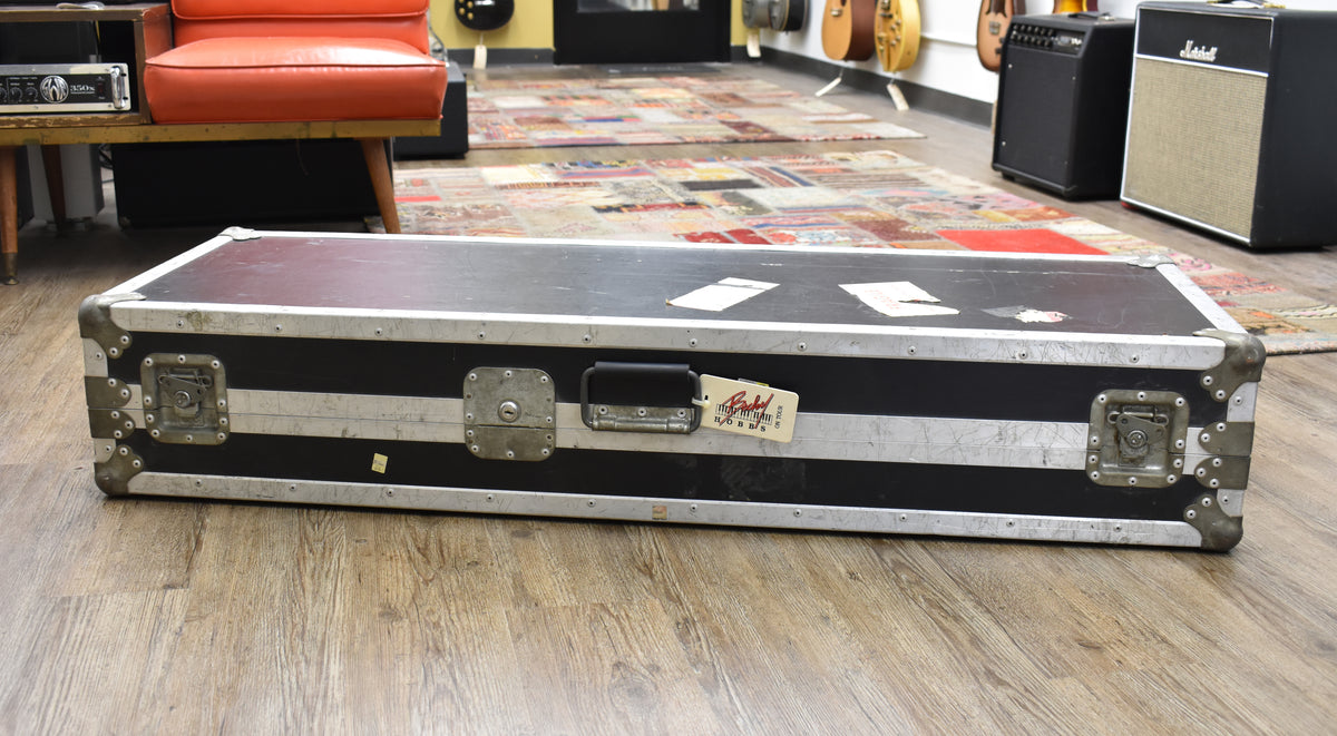 A black flight case with silver aluminum trim and hardware, showing wear, scuffs, and a tag on the handle.