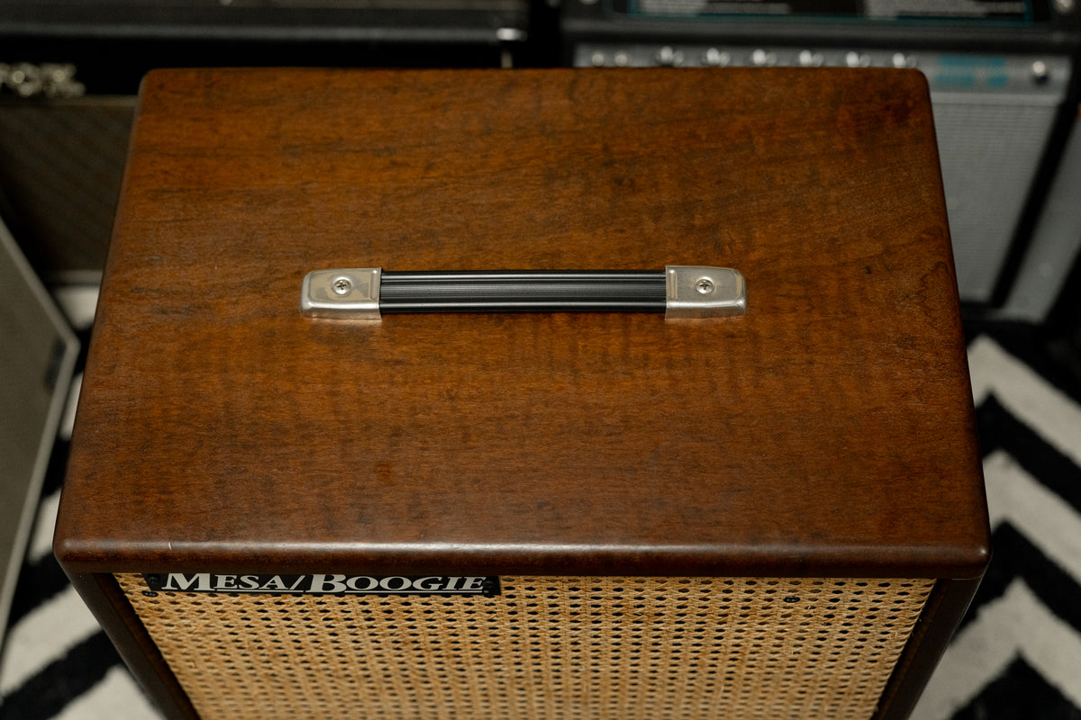 Top-down view of a dark brown wooden amp cabinet with a black handle, silver caps, and a light brown wicker grille.