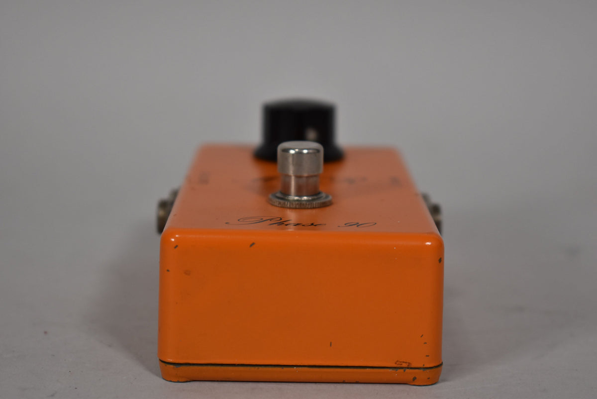 The orange pedal is viewed from the front, showing the silver footswitch and black knob, with minor chips and scratches.