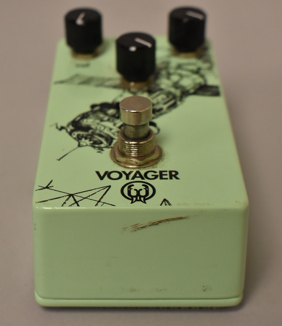 A light green effect pedal, angled from the front, showing three black knobs, a gold footswitch, and some scuffs on the right side.