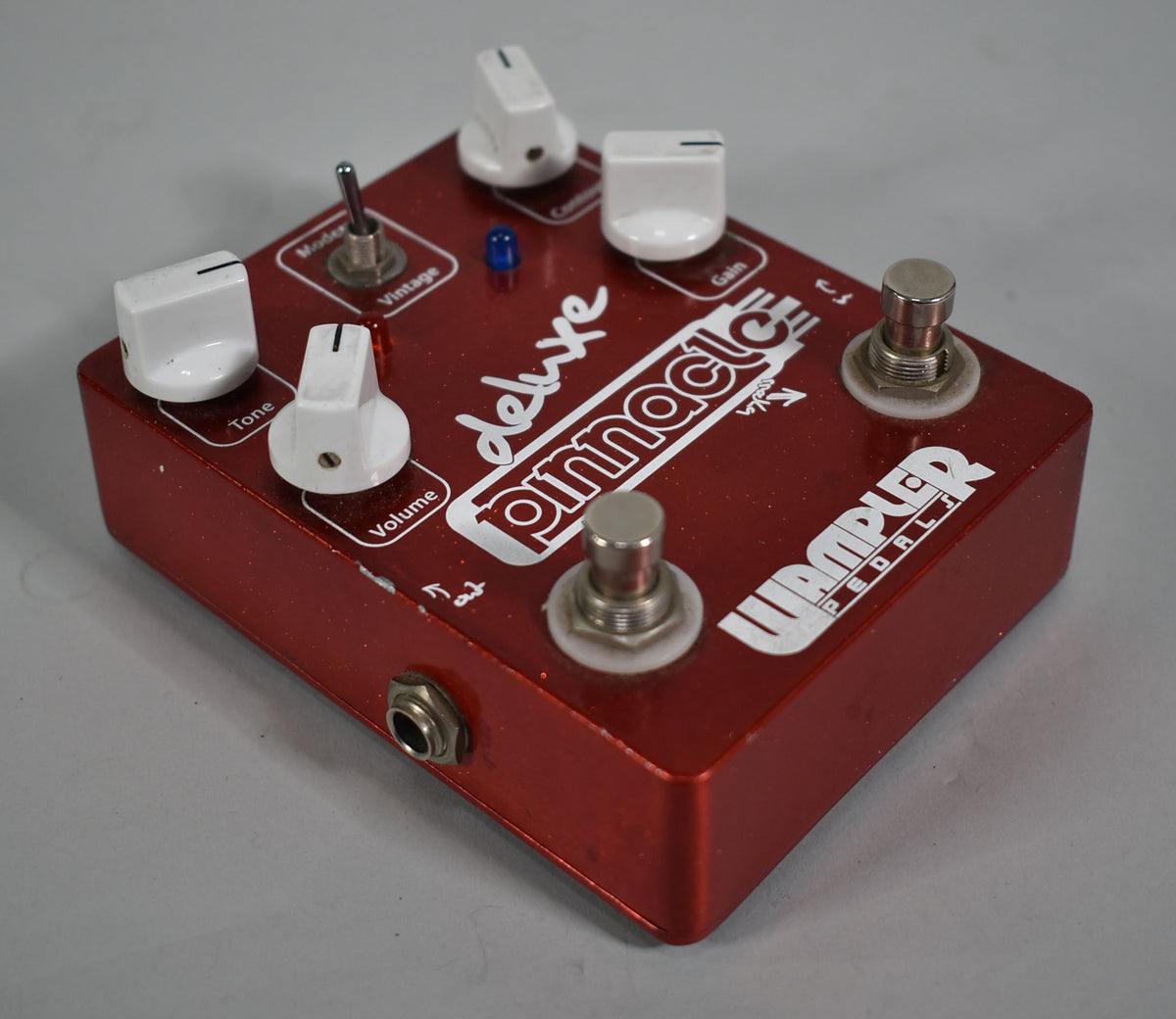 The red glitter-finish pedal is angled from the left, showing its top with five white knobs, a toggle switch, and two footswitches.