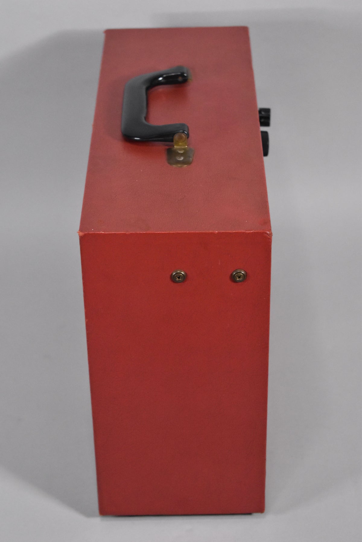 Top-down view of the red amp, showing the black handle with brass hardware, two black knobs on the side, and minor wear on edges.