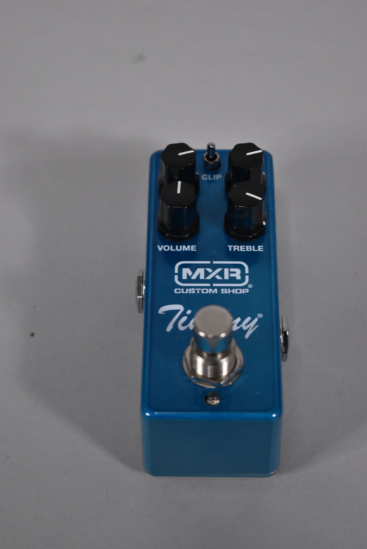A top-down view of a metallic blue pedal with four black knobs, a silver footswitch, and a small silver toggle switch.