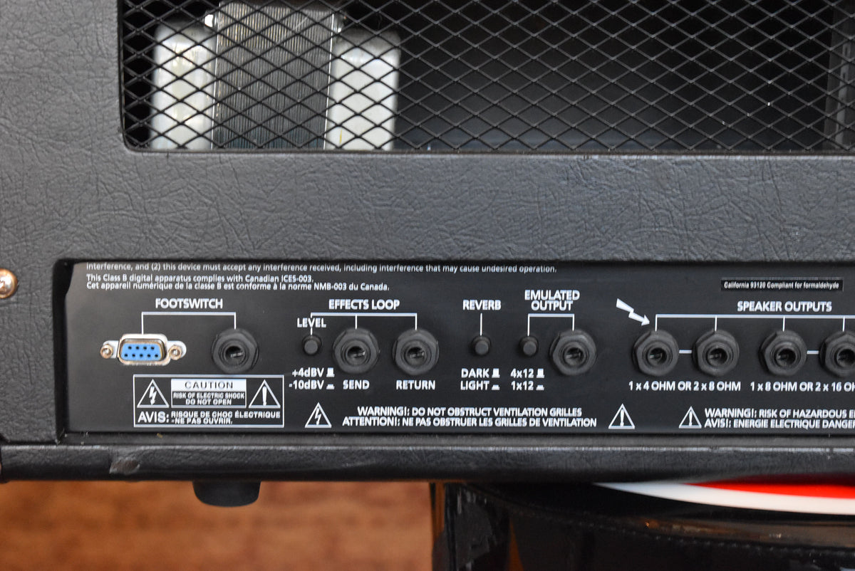 The amp's black rear panel shows a full array of inputs and outputs, including a blue footswitch port and multiple speaker outputs.