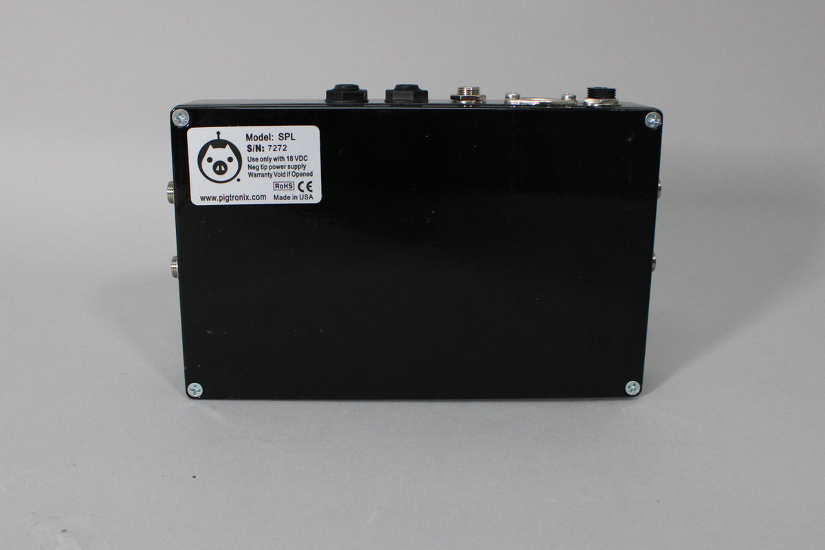 The black pedal is viewed from the rear, showing a white label, four silver screws, and several jacks along the top edge.