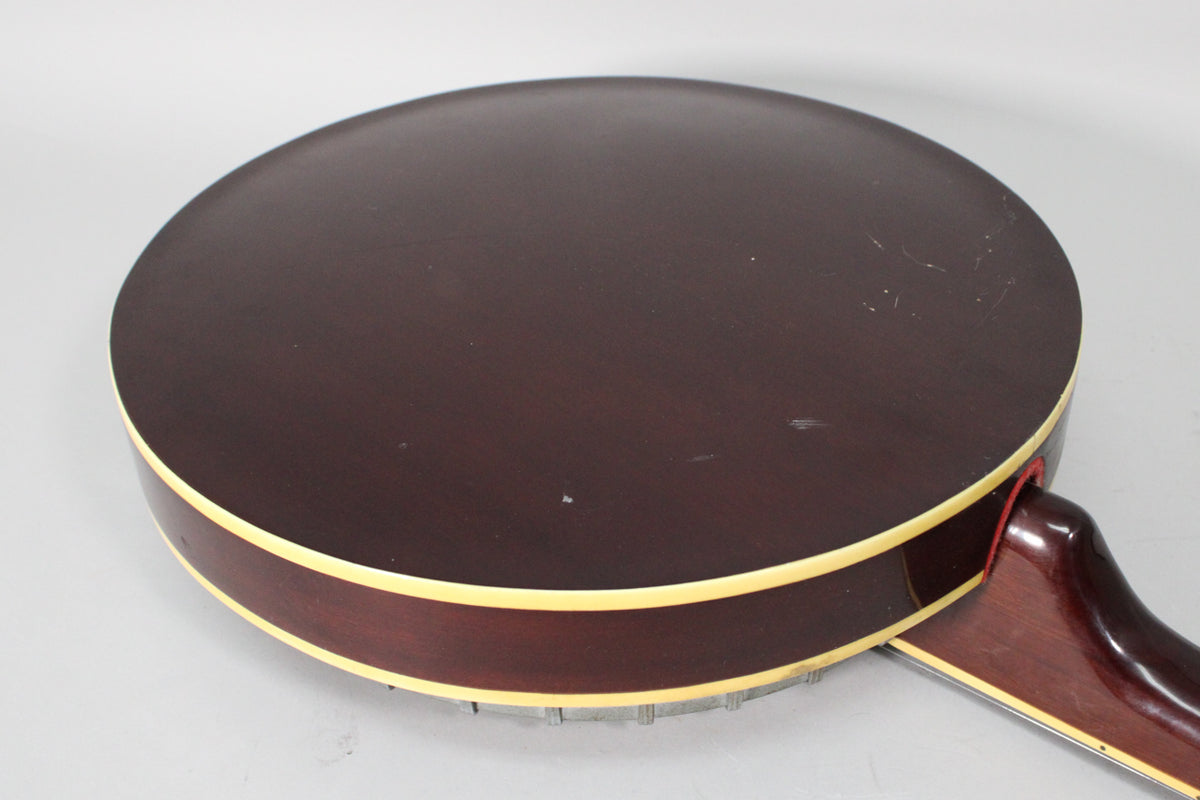 The banjo's dark brown resonator back, with cream binding, is shown from an overhead angle, revealing many scratches and scuffs.