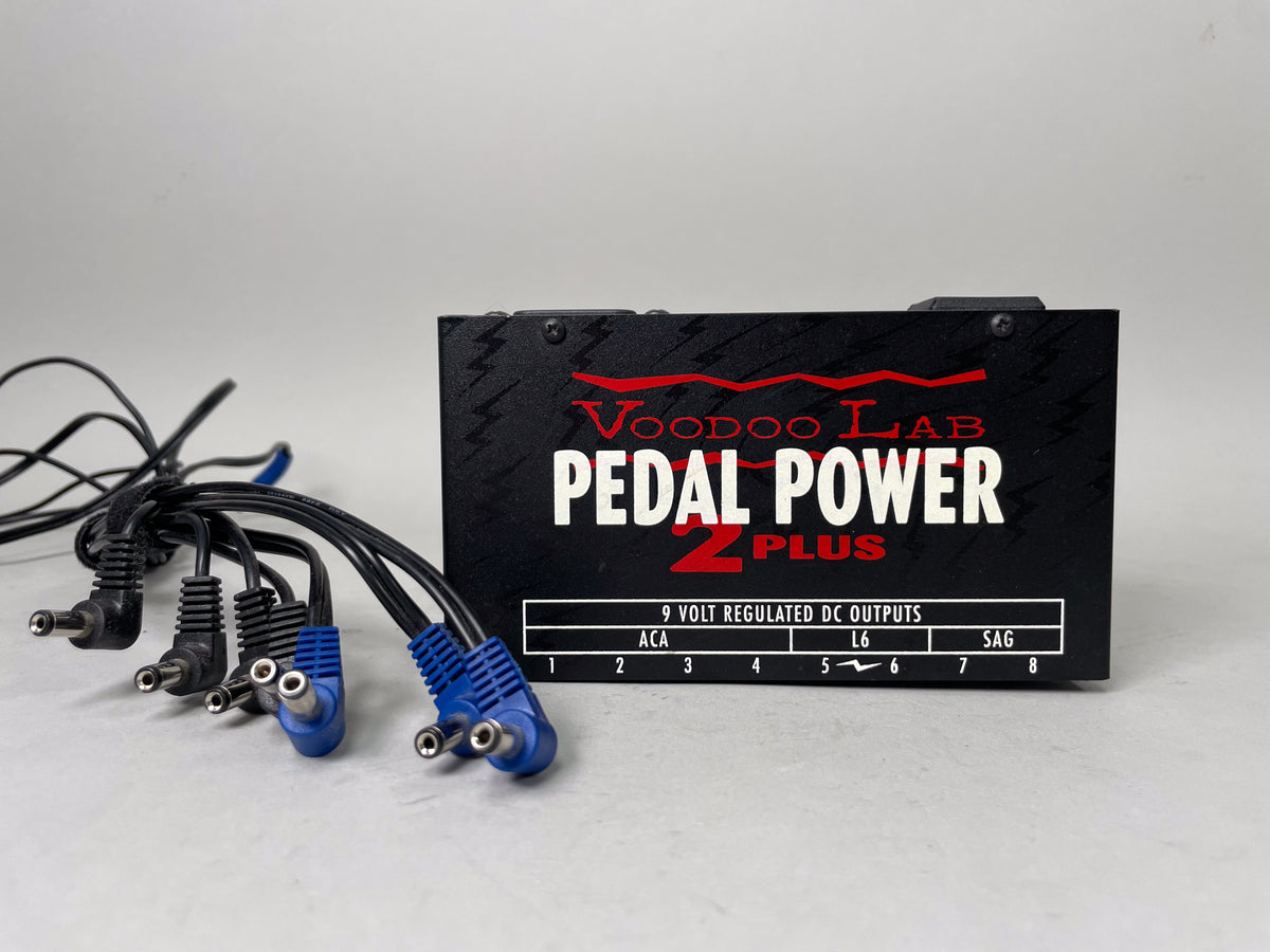 Black pedal power supply with red and white lettering, shown at an angle with multiple black and blue cables bundled to the left.