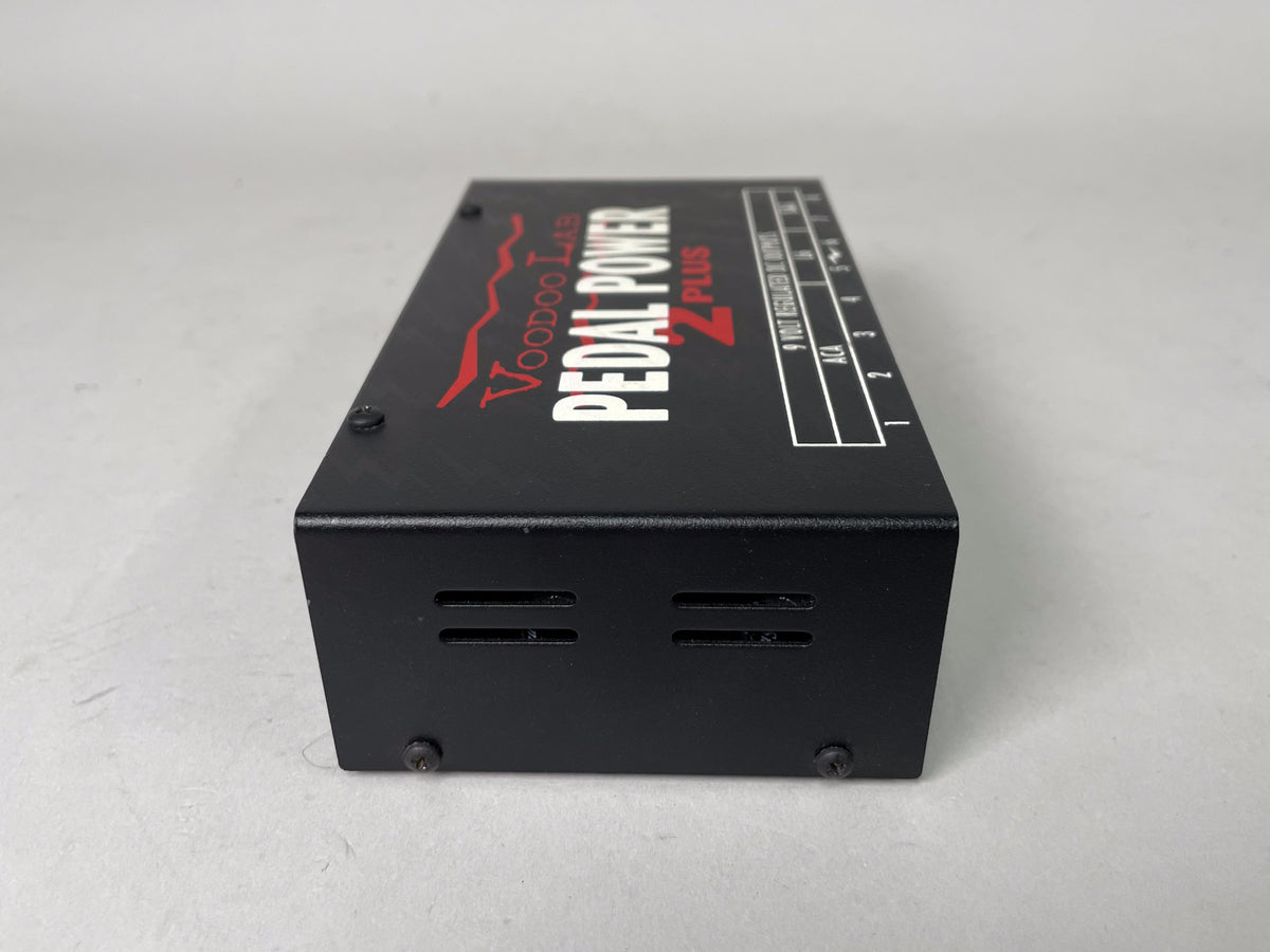 Black rectangular pedal power supply, angled from the front right, showing the top with red and white lettering and the right side with two vent slots.